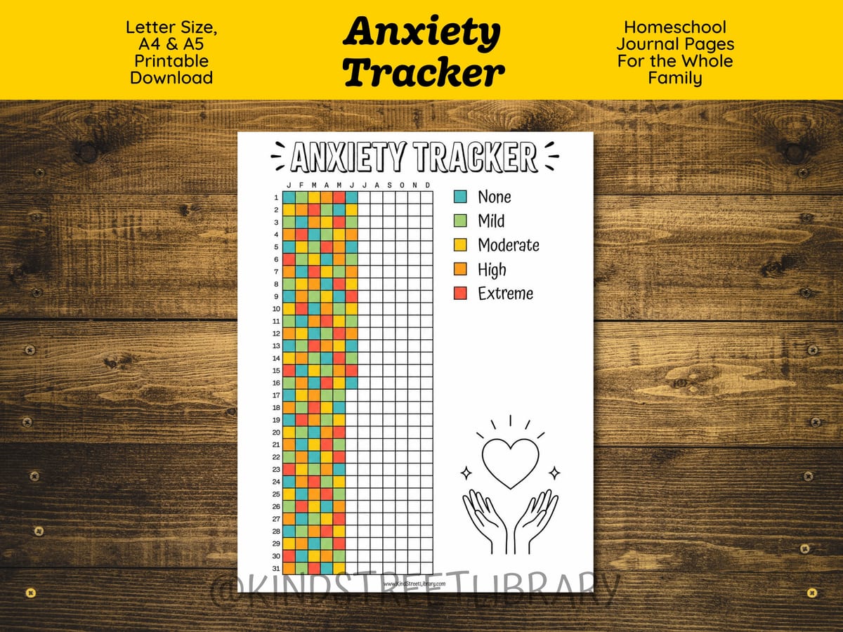 The Anxiety Tracker printable on a wooden table: a year-at-a-glance grid with one column per month, colored in teal, green, yellow, orange, and red squares from None to Extreme, beside a hand-drawn heart held in open hands